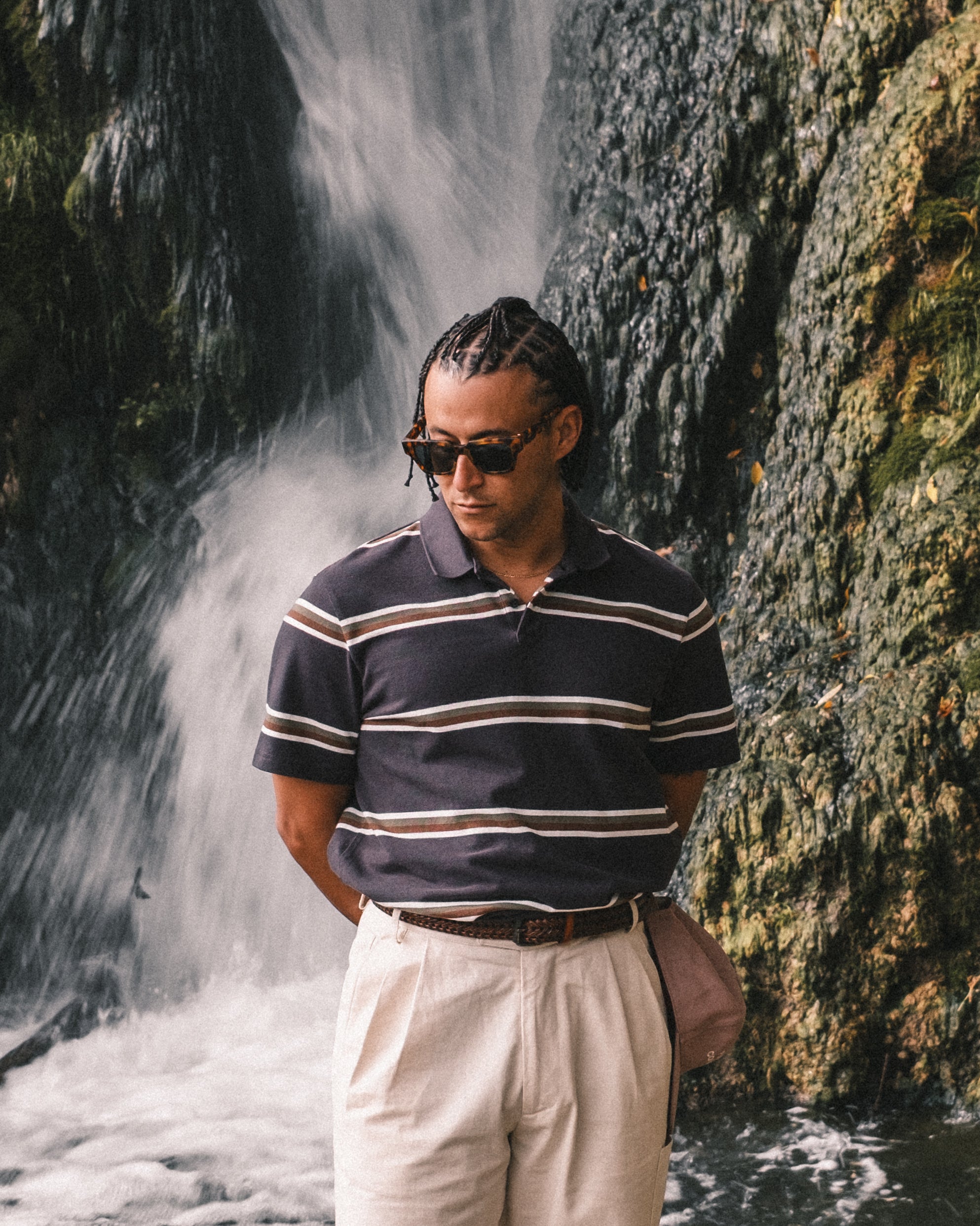 Man wearing a striped polo shirt and sunglasses standing in front of a waterfall.