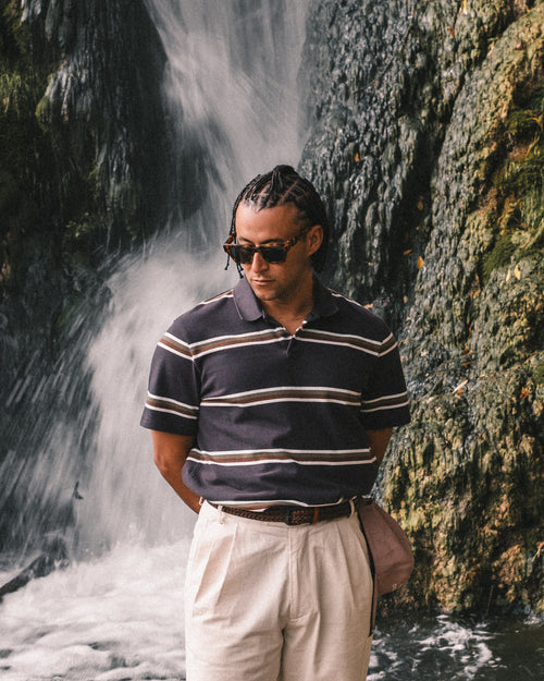 Man wearing a striped polo shirt and sunglasses standing in front of a waterfall.
