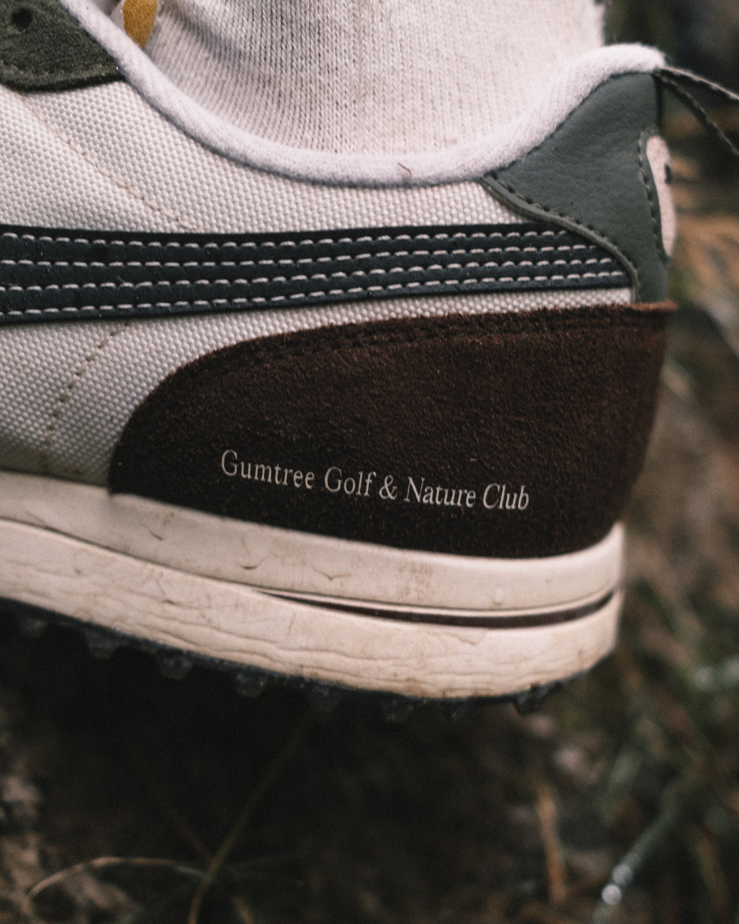 Close-up of a shoe with 'Gumtree Golf & Nature Club' branding on a natural background.
