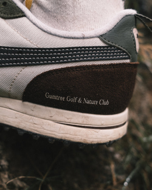 Close-up of a shoe with 'Gumtree Golf & Nature Club' branding on a natural background.