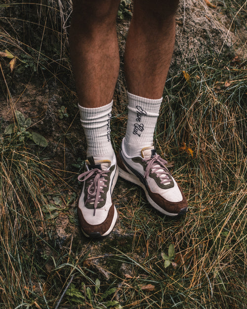 Person wearing white socks with text and brown and white sneakers standing on grass.