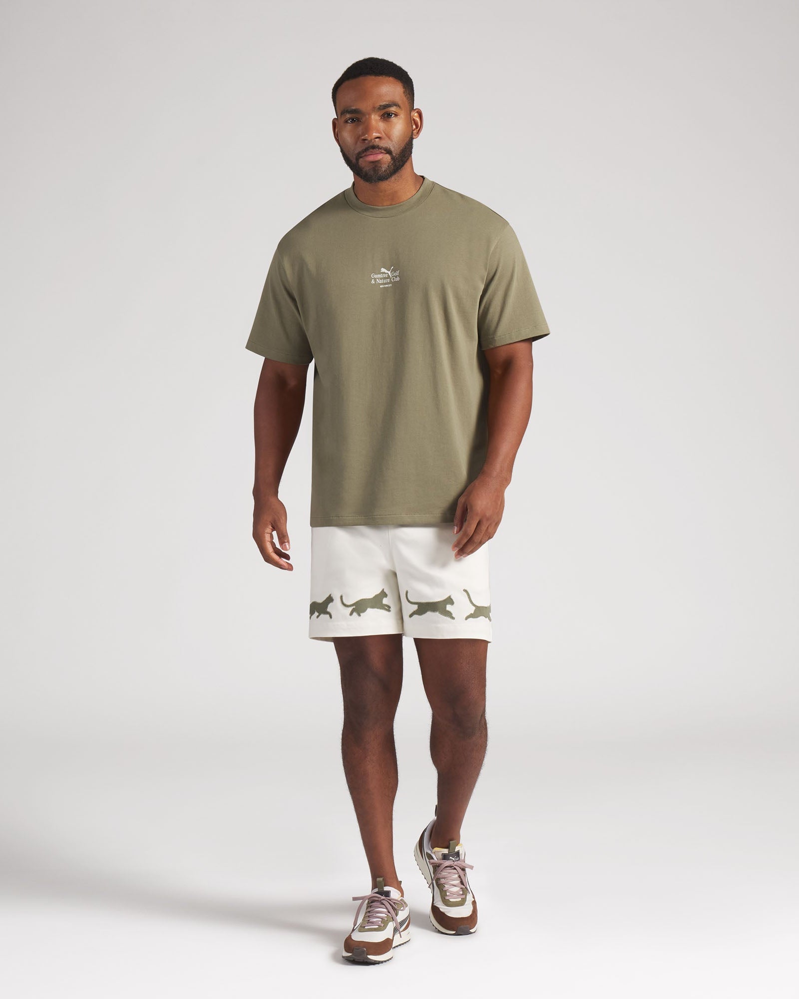 Man wearing a green t-shirt and white shorts with animal prints on a plain background