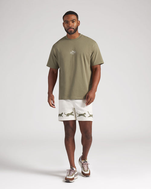 Man wearing a green t-shirt and white shorts with animal prints on a plain background