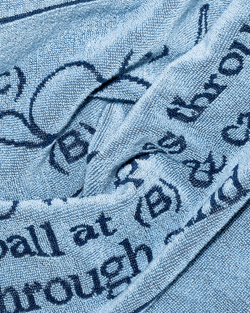 A close-up of a light blue textured fabric, likely a towel or blanket, printed with dark navy blue text and graphic elements.