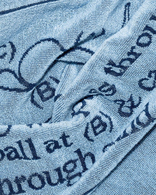 A close-up of a light blue textured fabric, likely a towel or blanket, printed with dark navy blue text and graphic elements.