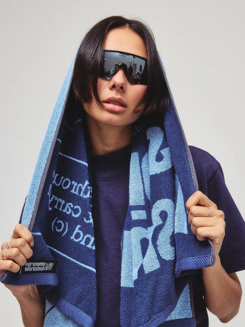 Person holding a blue towel with text and graphics, wearing sunglasses and a dark shirt.
