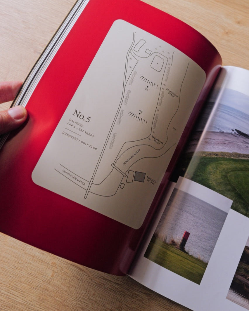 Open book with a red cover and beige page featuring a map and text, held by a hand on a wooden surface.