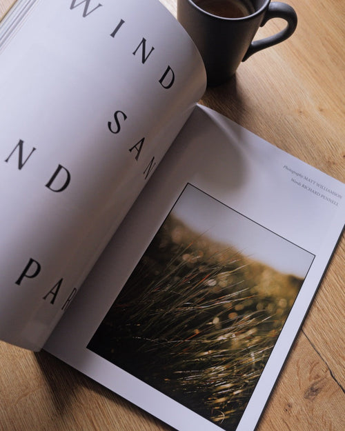 Open book with a photograph of a sunset on a wooden surface next to a cup of coffee.