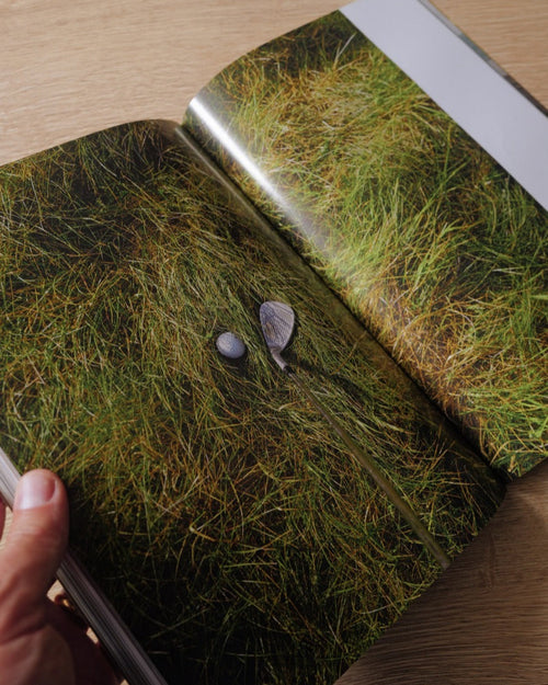 Open book showing a photograph of grass and stones on a wooden surface